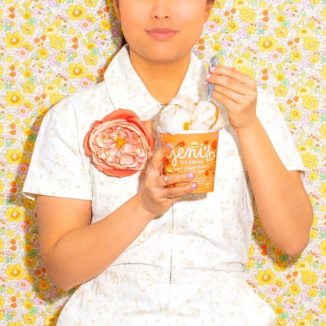 a model standing against a floral wall eating a pint of jeni&#x27;s ice cream
