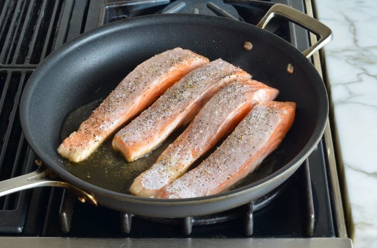 Four salmon fillets in a skillet cooking skin side up.