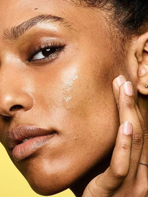 A model with dark skin rubbing the clear sunscreen onto their cheek with no visible residue 