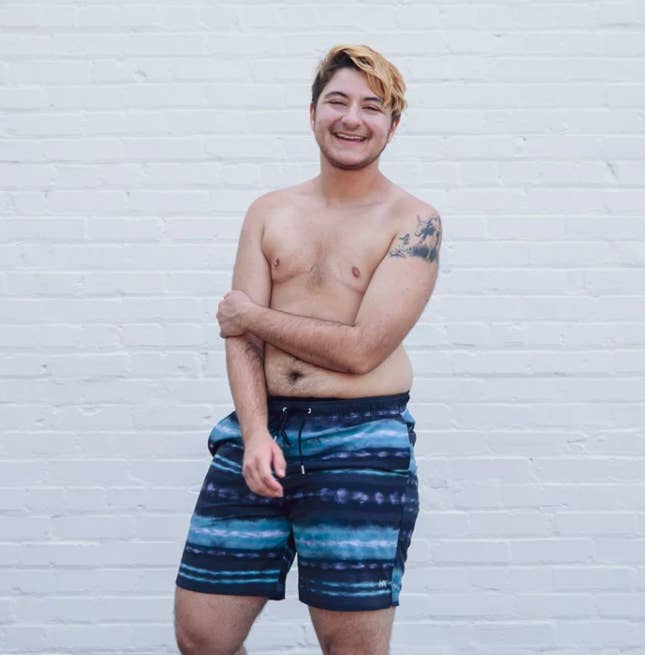 Model wears Humankind Swim navy blue swim trunks with a blue and white lined pattern
