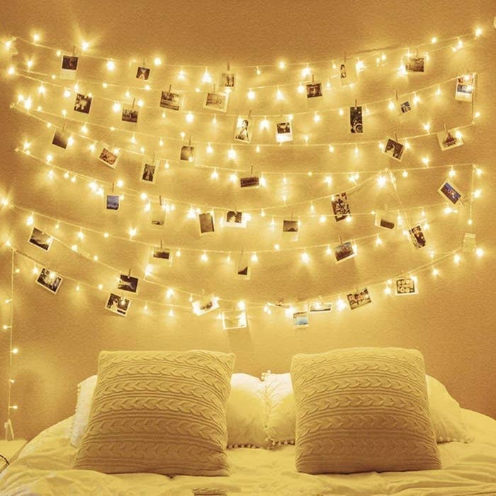 Fairy lights are strung up above a bed with pictures attached to the cord with clothespins 