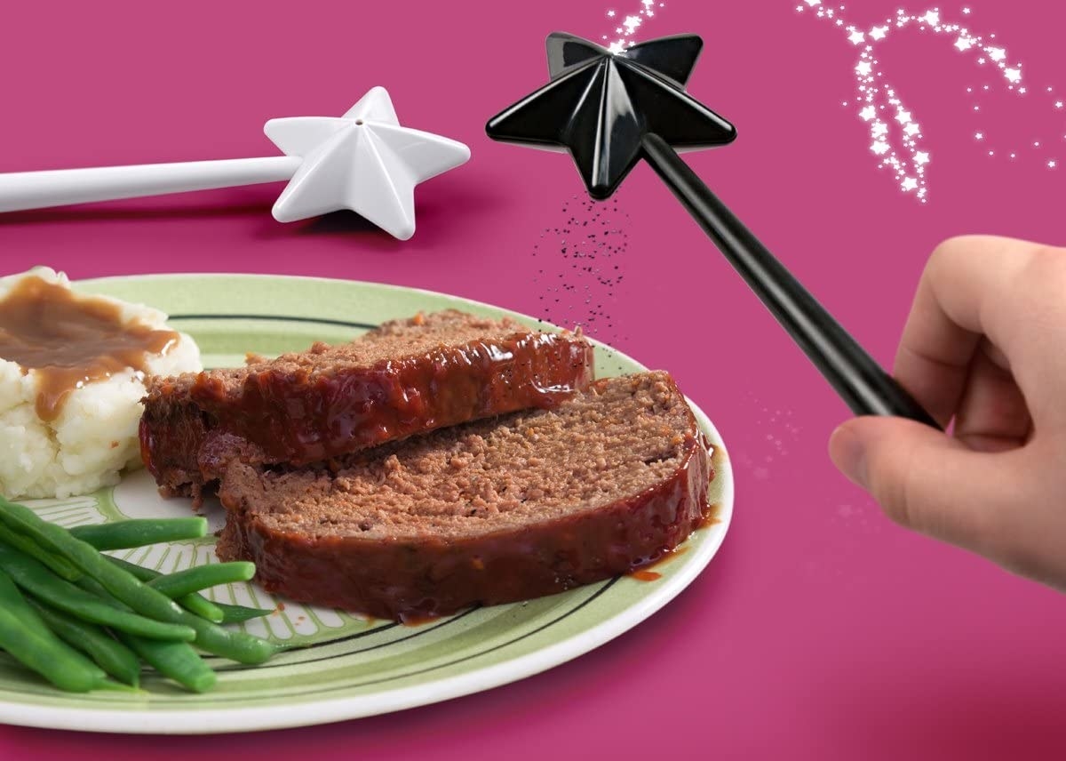 Salt and pepper wands being used to season a plate of meatloaf, mashed potatoes, and beans