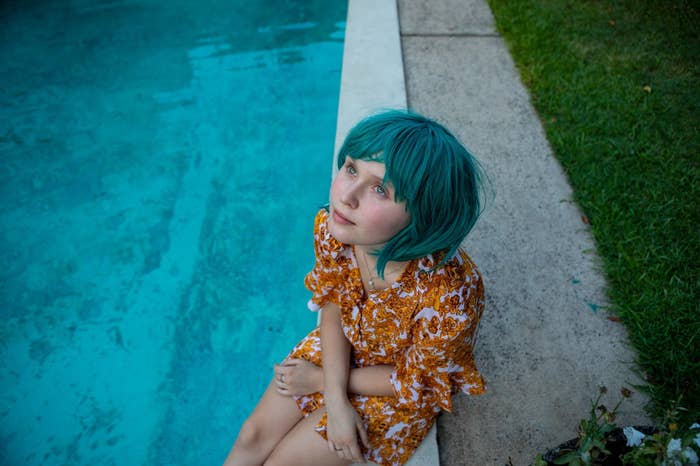 一个十几岁的女人坐在游泳池旁边,身穿绿色假发。