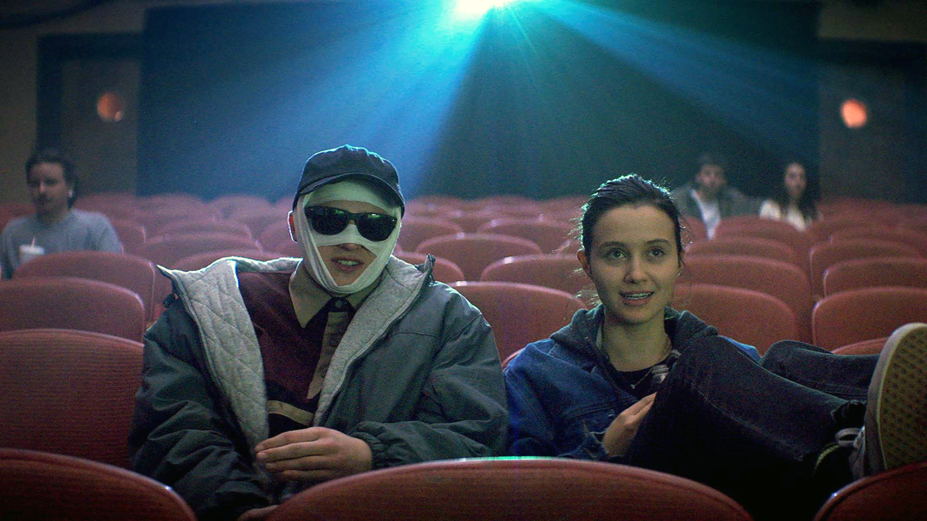 绷带的男人他的脸在电影院和一个女孩坐在他旁边。