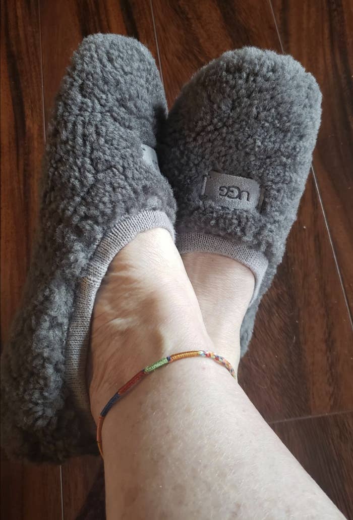 A reviewer&#x27;s feet wearing the slippers which have shearling wool all over them. They fit and look like ankle socks but are thicker.