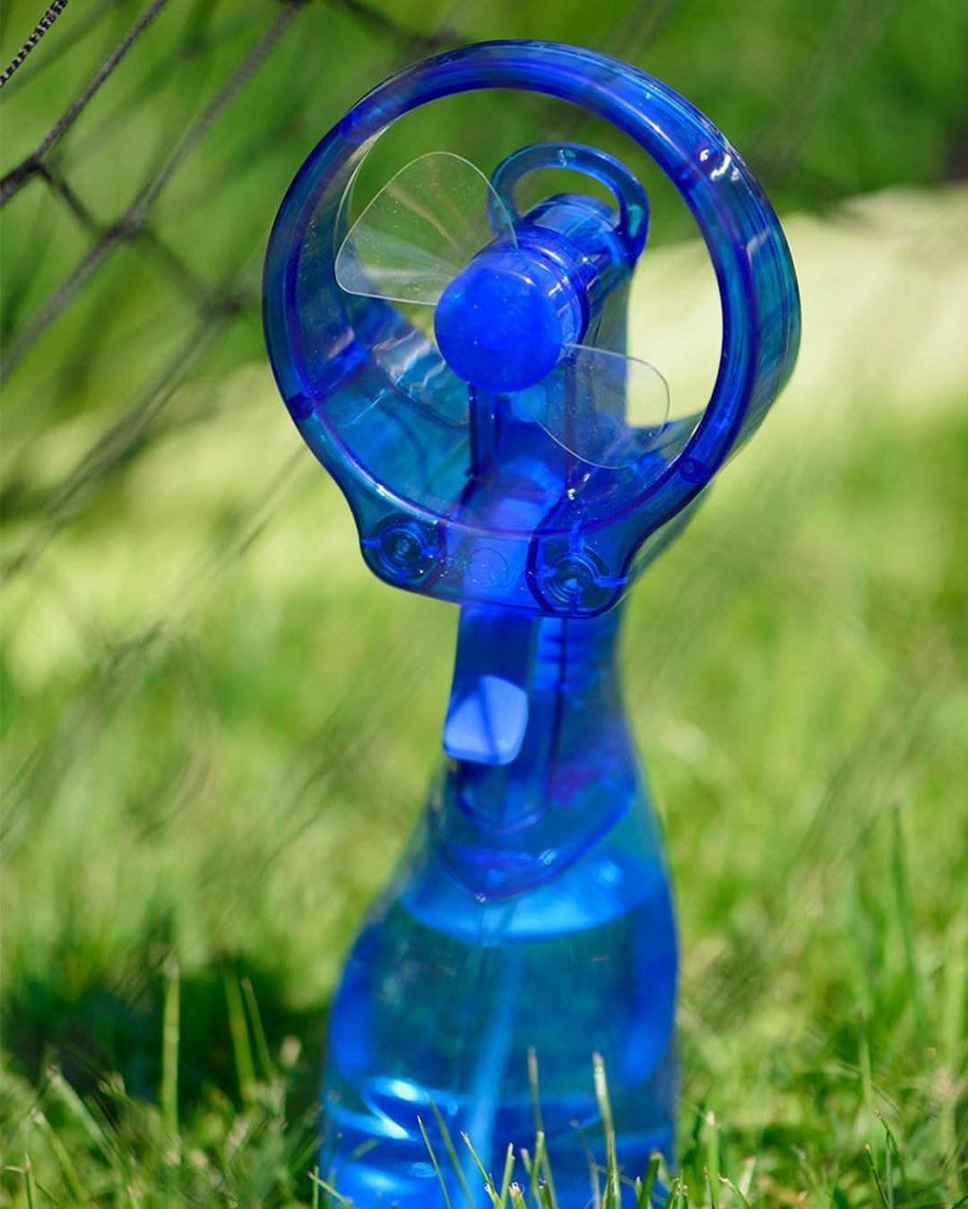 A bottle filled with water with a fan attachment is placed upright on grass