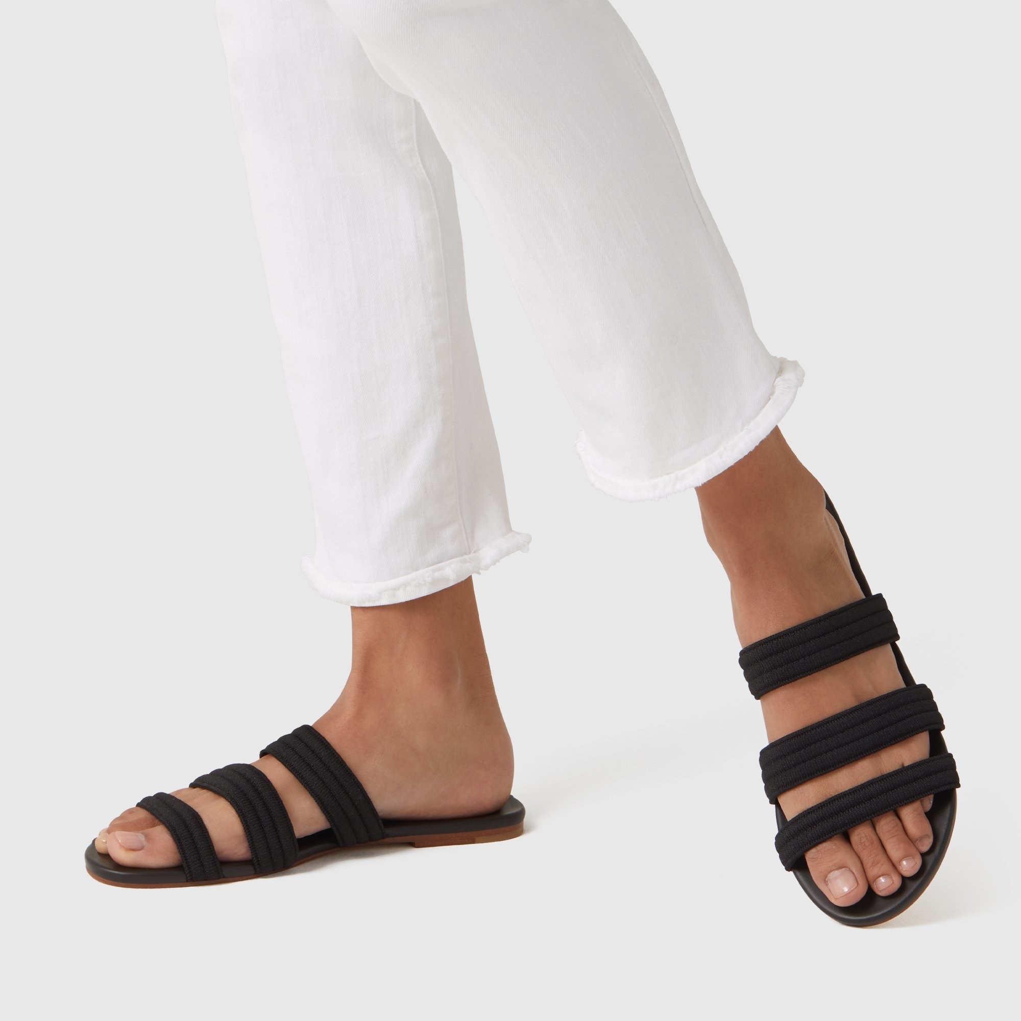 Model wearing the sandals in black with three knit straps across the food