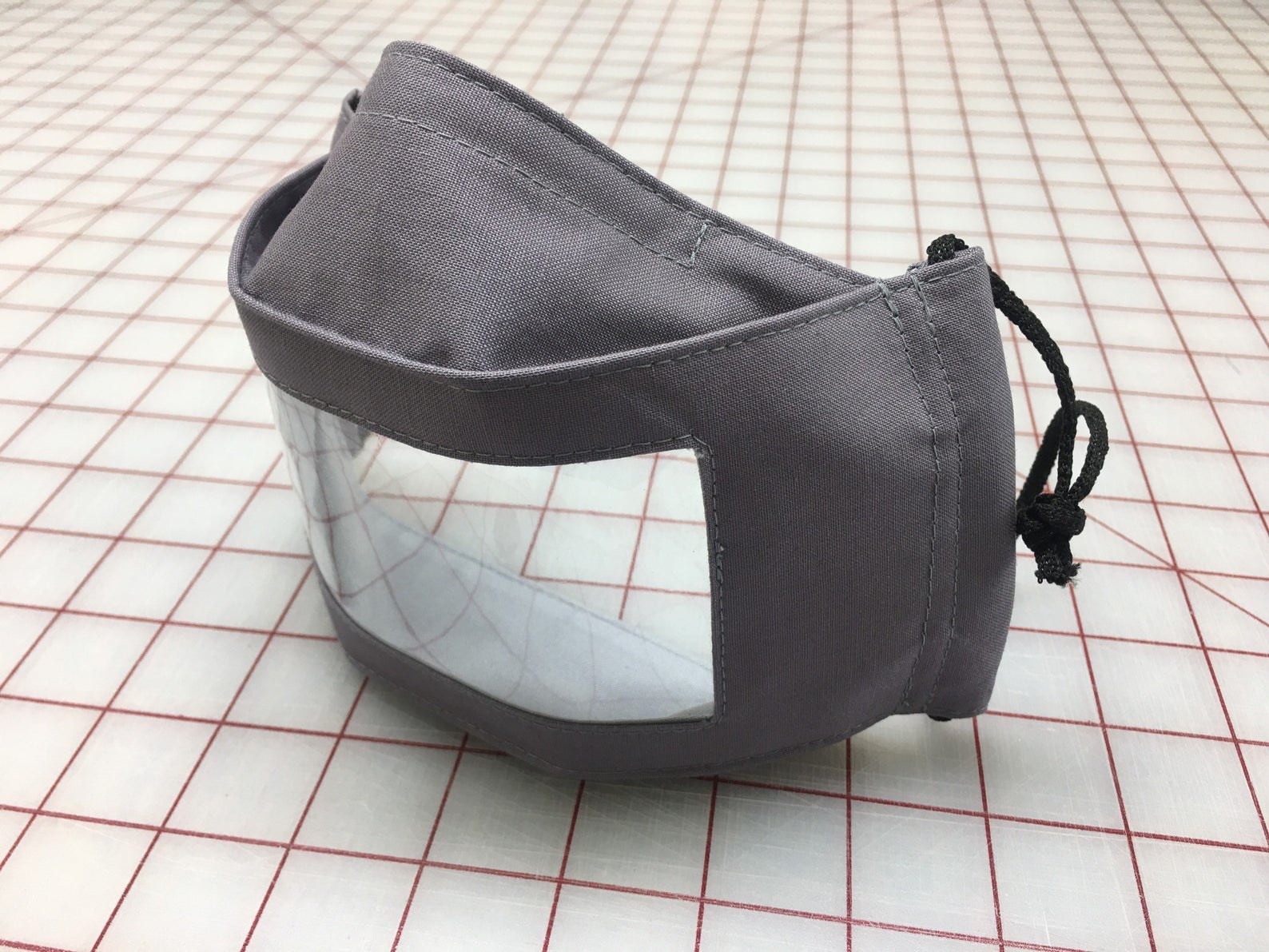 A gray face mask with plastic window in it  that allows other people to see the wearer&#x27;s mouth 