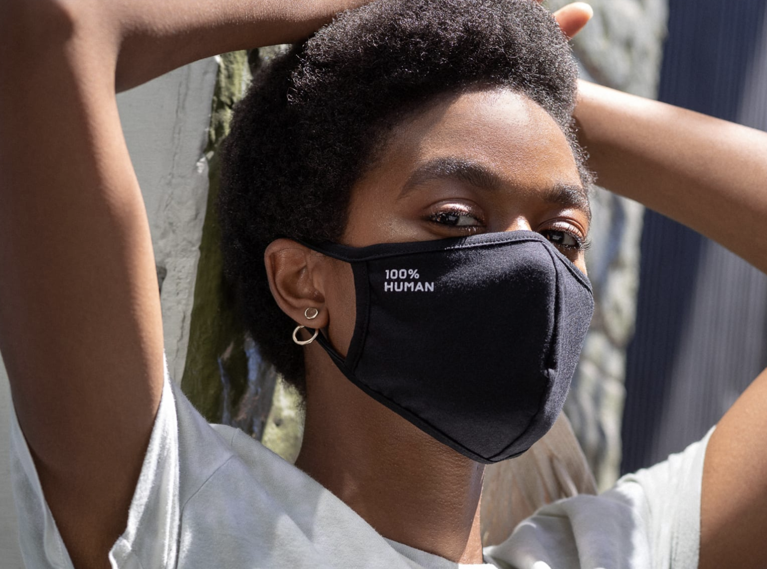 A model in a black face mask with a &quot;100% Human&quot; logo on the upper left side