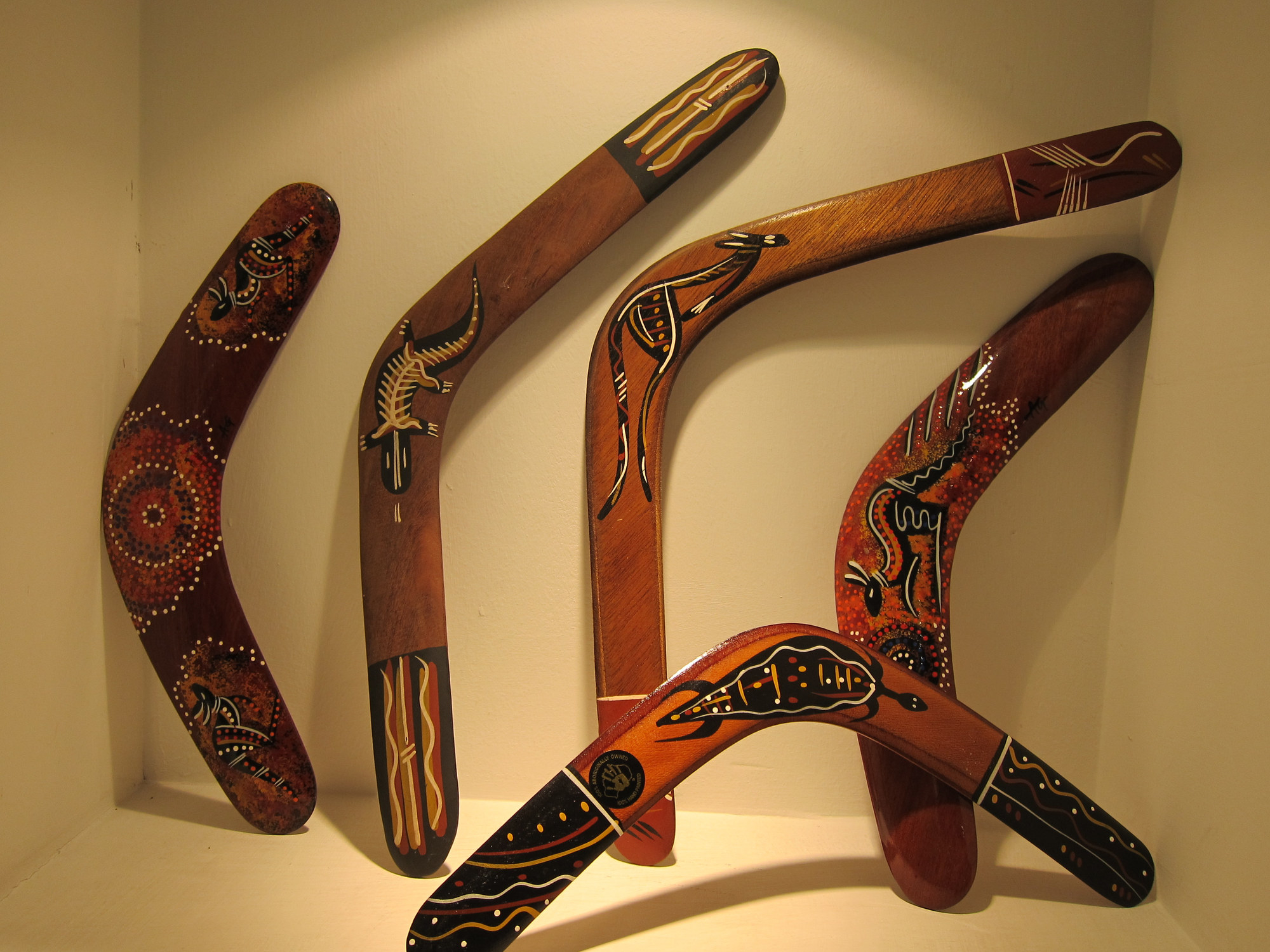 A display of five wooden boomerangs with artwork