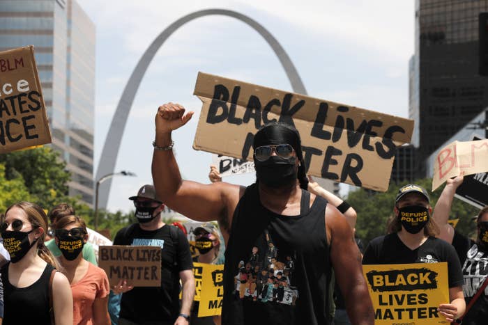 People march in front of the Gateway Arch holding Black Lives Matter signs