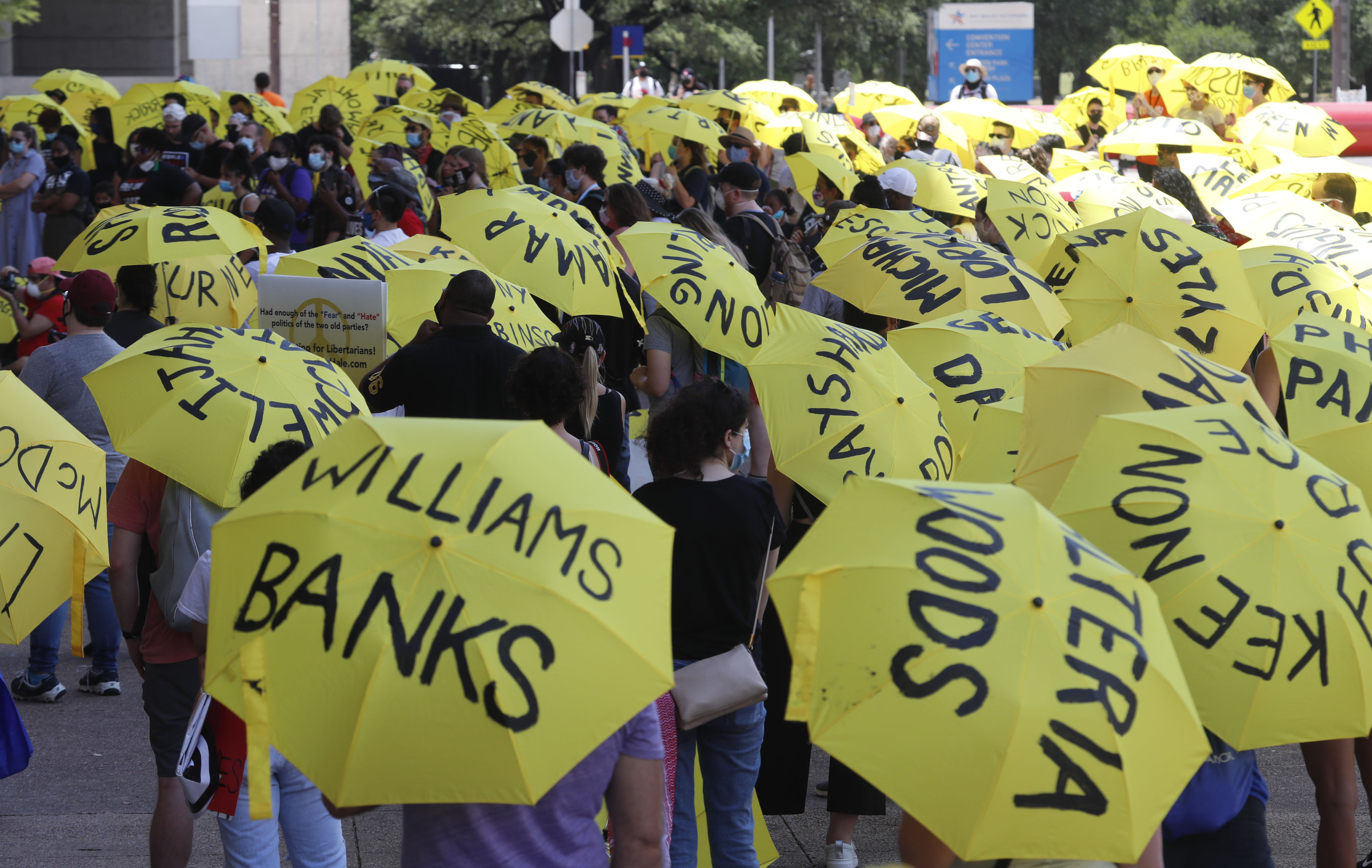 People hold yellow umbrellas marked with the names of people killed in police custody