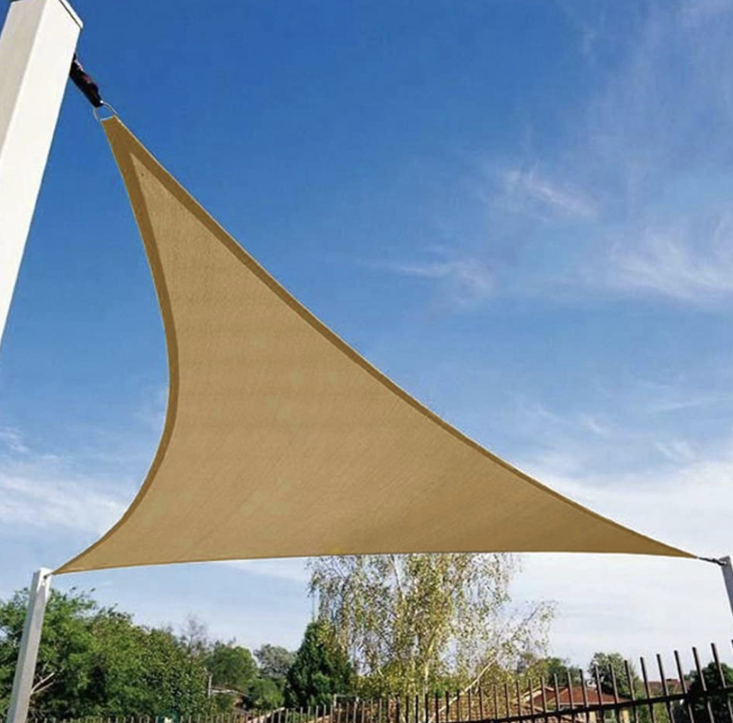 A tan sunshade triangle covers a backyard near a fence