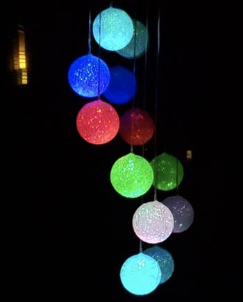 The same solar wind chime glowing at night with light blue, dark blue, green, and red balls