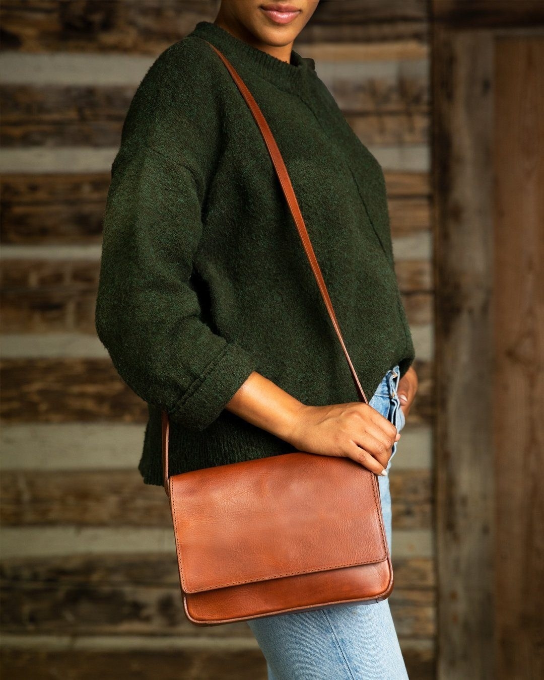 Model wearing cross-body purse with front flap over their shoulder in brown
