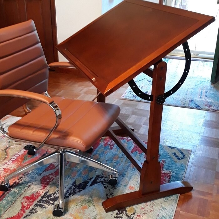 A brown wood drafting table angled at 45-degrees