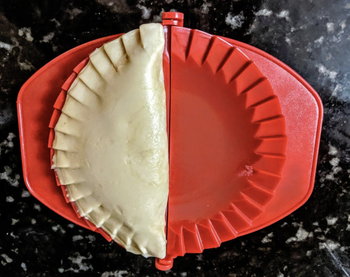 An uncooked empanada in one of the dough presses after being shaped