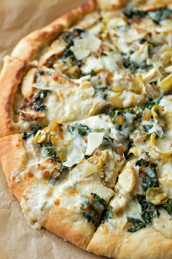 A pizza with spinach artichoke sauce cut into slices.