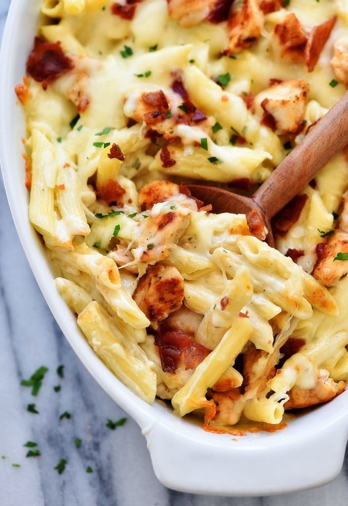 A wooden spoon scooping into a baking dish full of cheesy baked chicken ranch pasta.