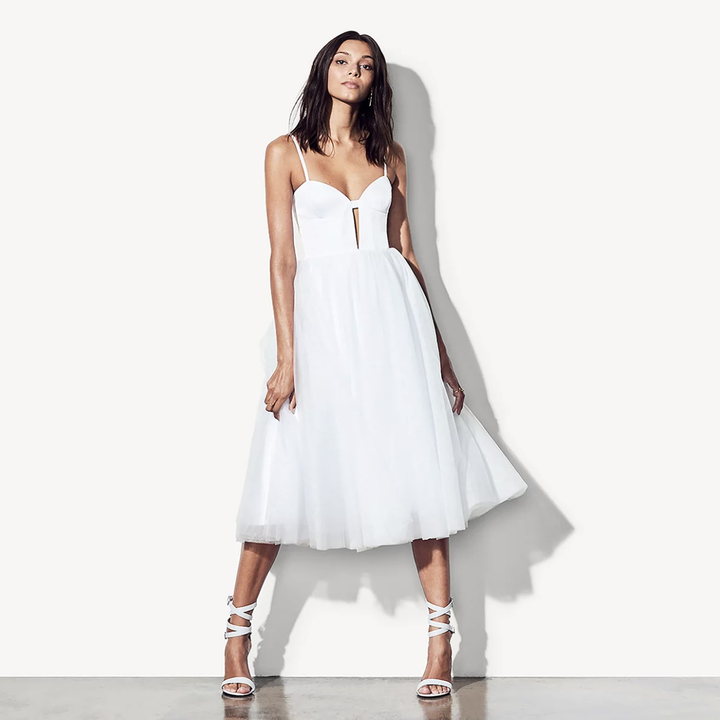 a model wearing a mid length dress with a structured bodice made of white matte satin, thin straps, and a tulle skirt