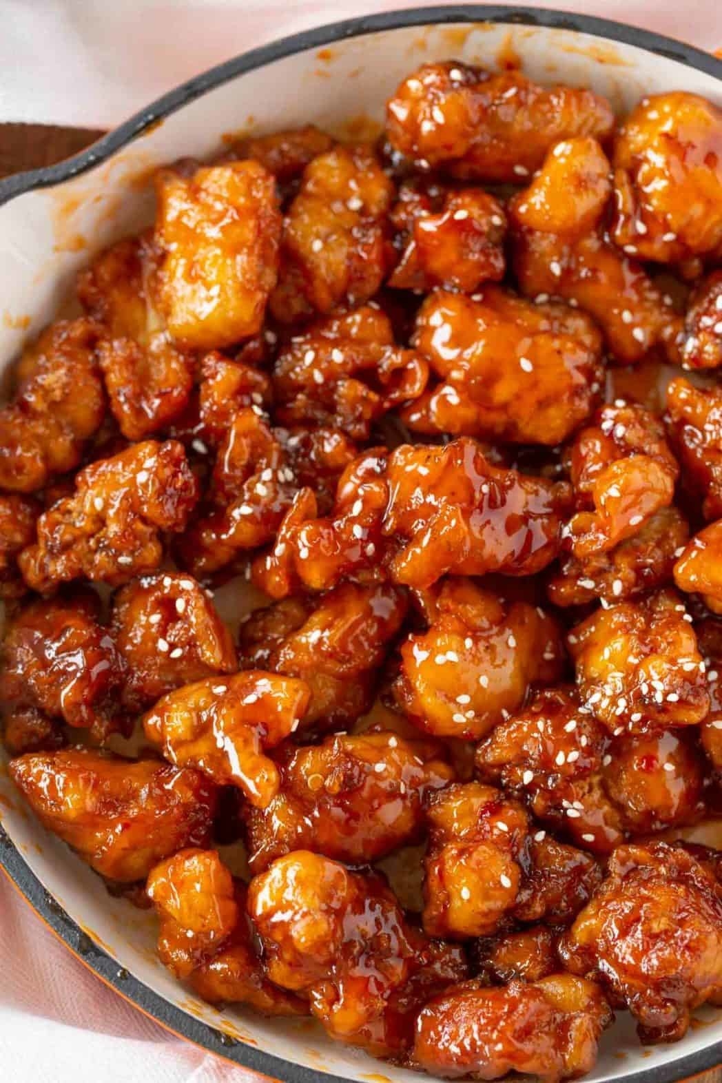 A Dutch oven full of crispy sesame chicken tossed in a sticky glaze and sesame seeds.