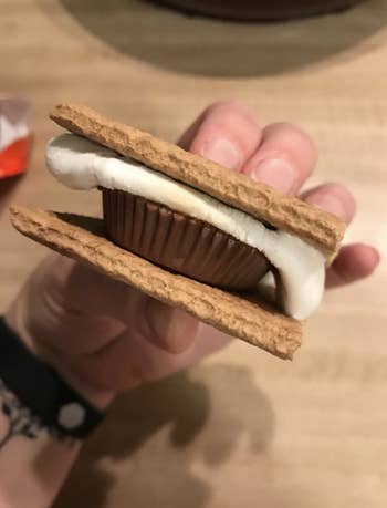 A reviewer holding up a s'more with a Reese's peanut butter cup inside of it 