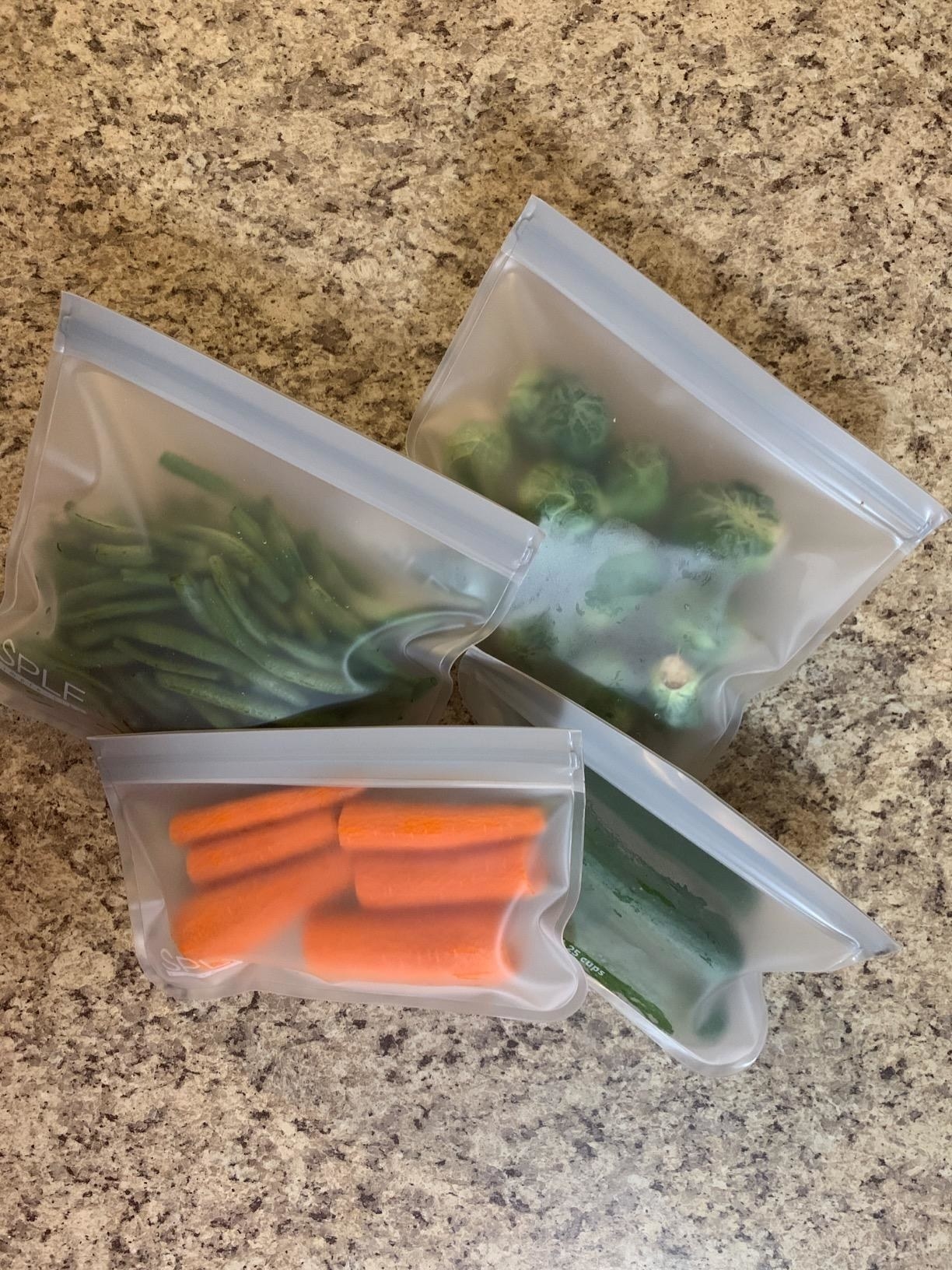 A review image of four baggies with carrots, string beans, Brussels sprouts, and cucumbers in them