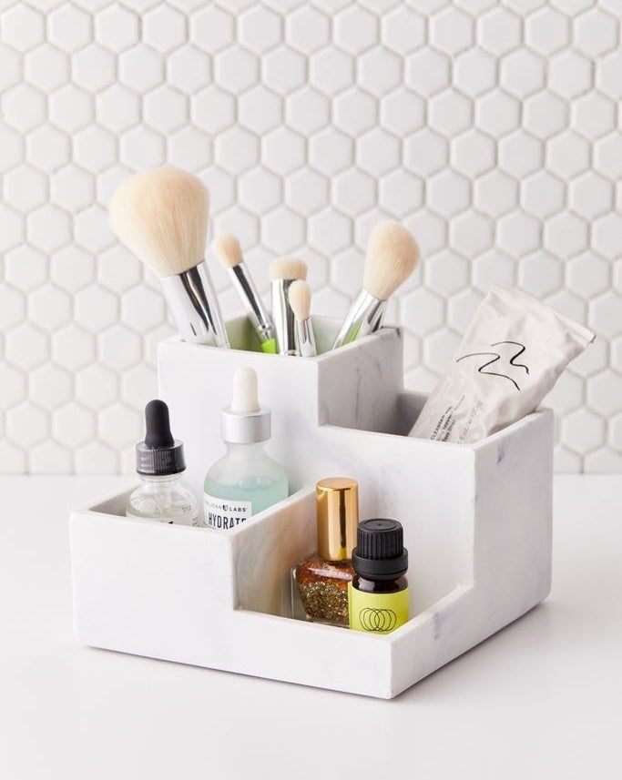 A cube tray with four square storage spots placed at different heights. One has room for brushes, another toothpaste, and the last two are large enough for nail polish and small serum bottles 