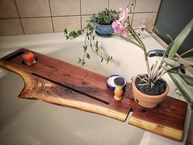 An Etsy shop owner's photograph of their wood caddy, with a slot for and iPad, a smartphone, and a cup holder. The wood is a flat piece that's long enough to extend past both sides of the tub.