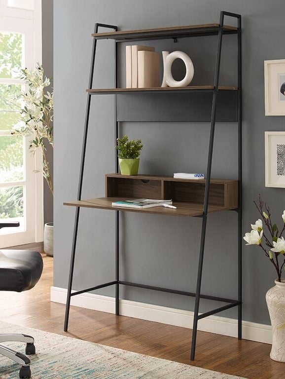 A ladder desk with a thin black metal, wooden shelves, and a cubby