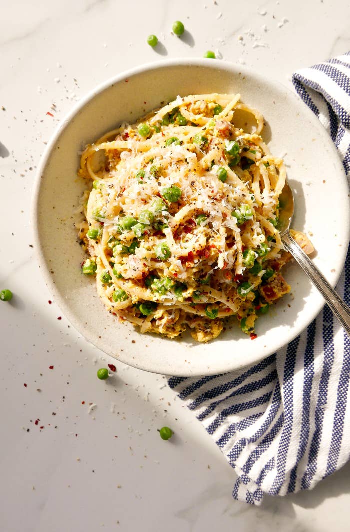 A bowl of creamy spaghetti carbonara with pancetta, peas, and grated Parmesan.