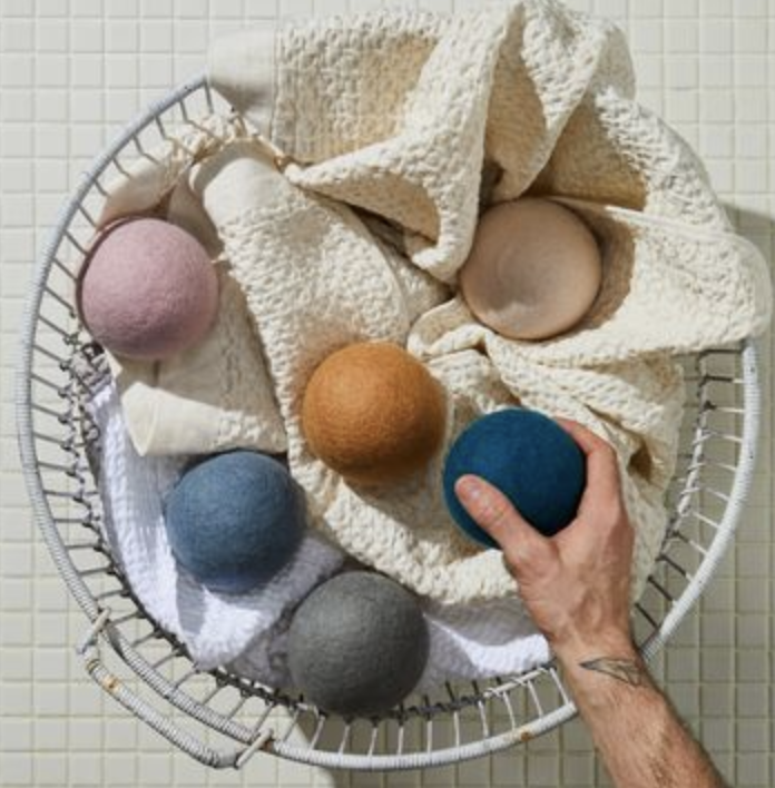 A model holds a blue dryer ball above a laundry bin filled with towels