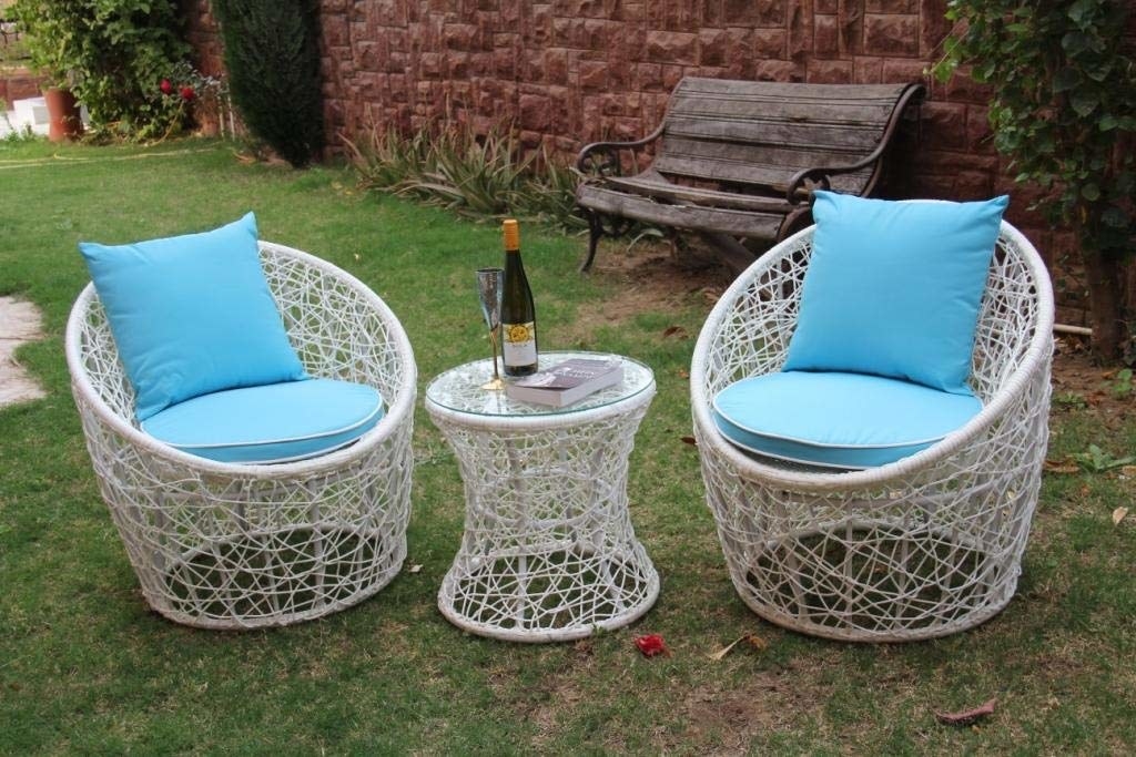 Two wicker chairs with blue seat cushions and pillows with a round table between them.