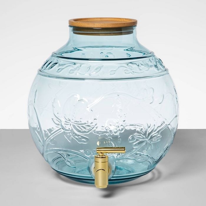 a clear jug with a blue tint and floral design on it and a gold spout attached