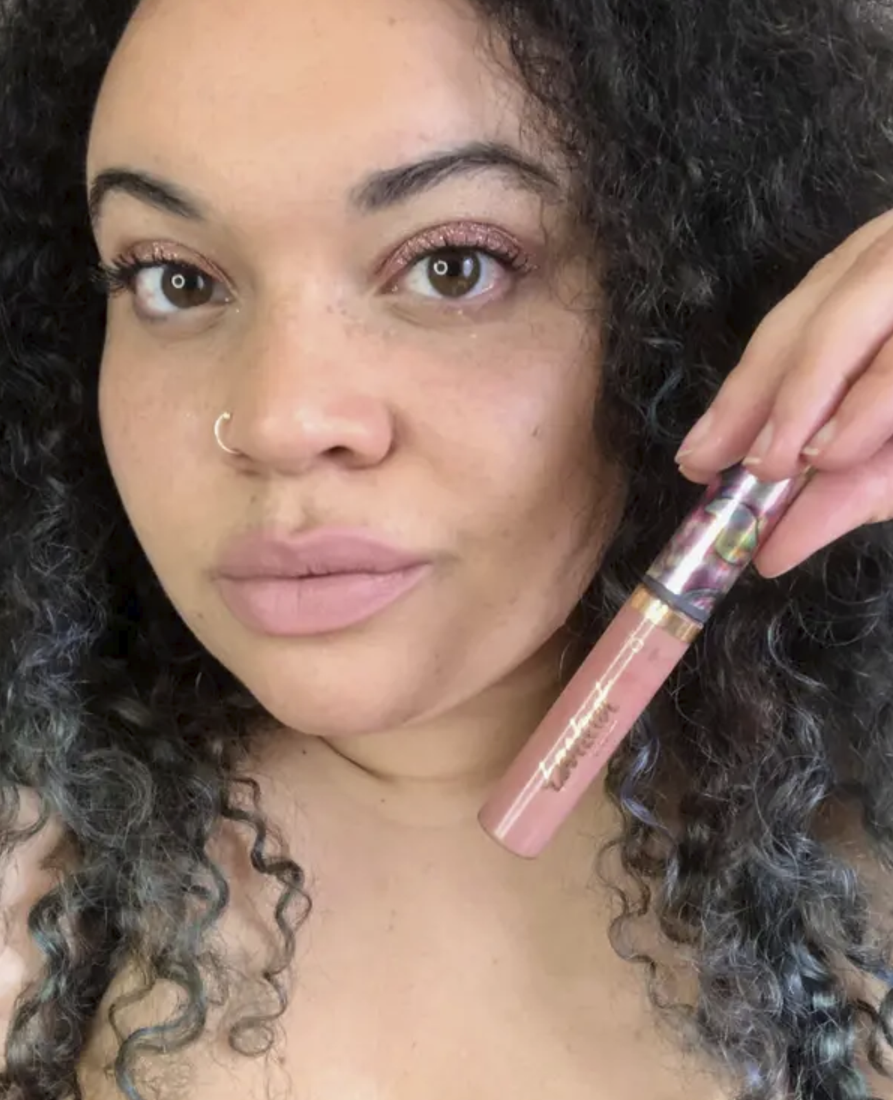 BuzzFeed editor wearing a nude pink lipstick and holding the tube near her face