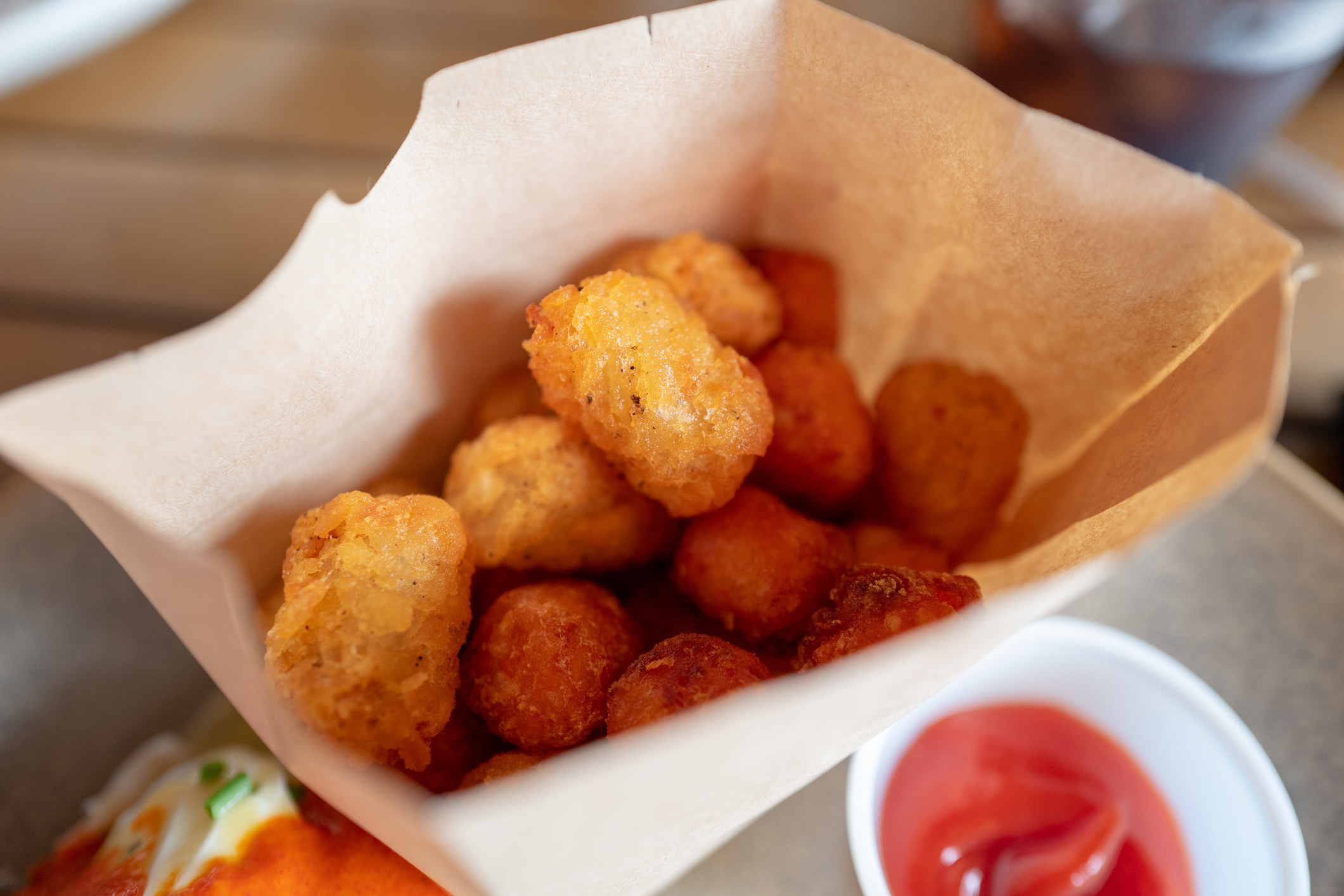 Paper bag filled with crispy tater tots and a side of ketchup