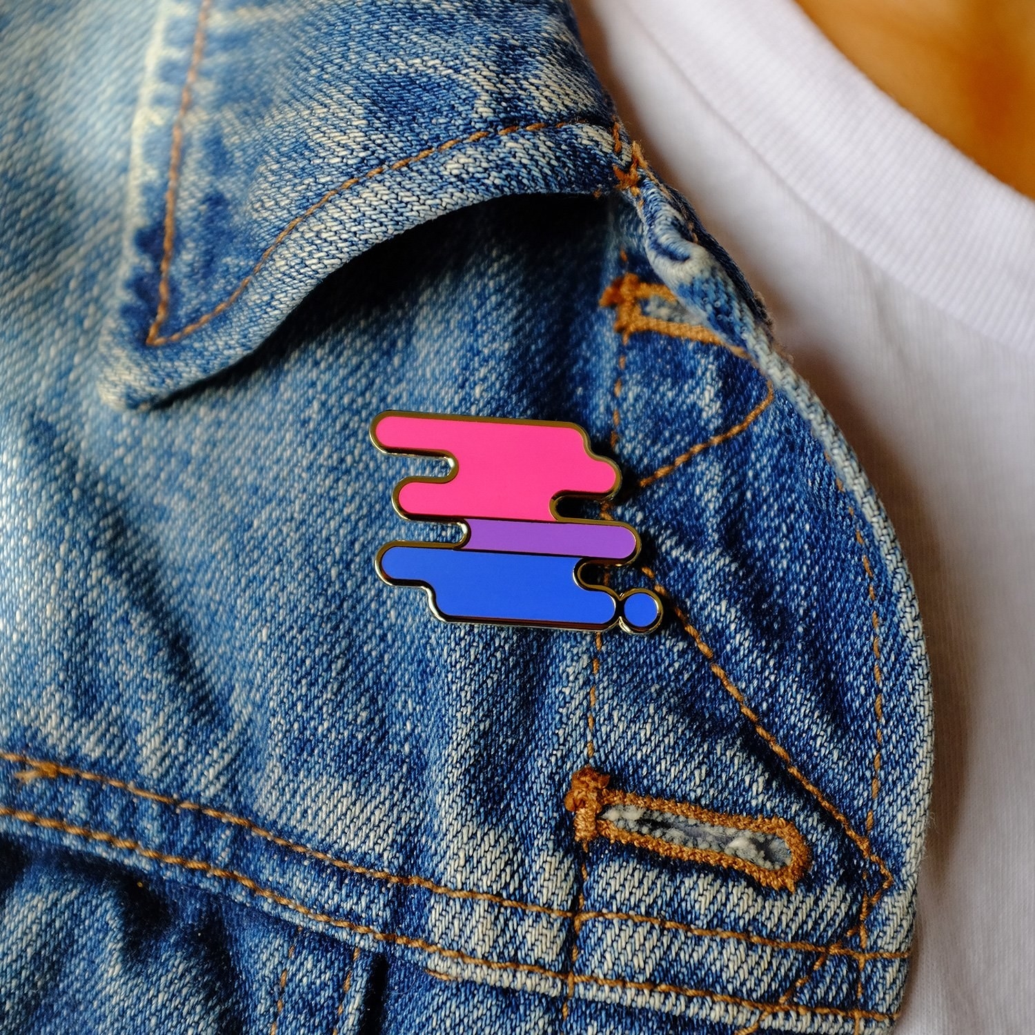 A bisexual pride pin pinned to a denim jacket