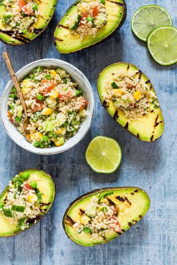 Avocado halves on a wooden surface filled with vegetable quinoa salad.