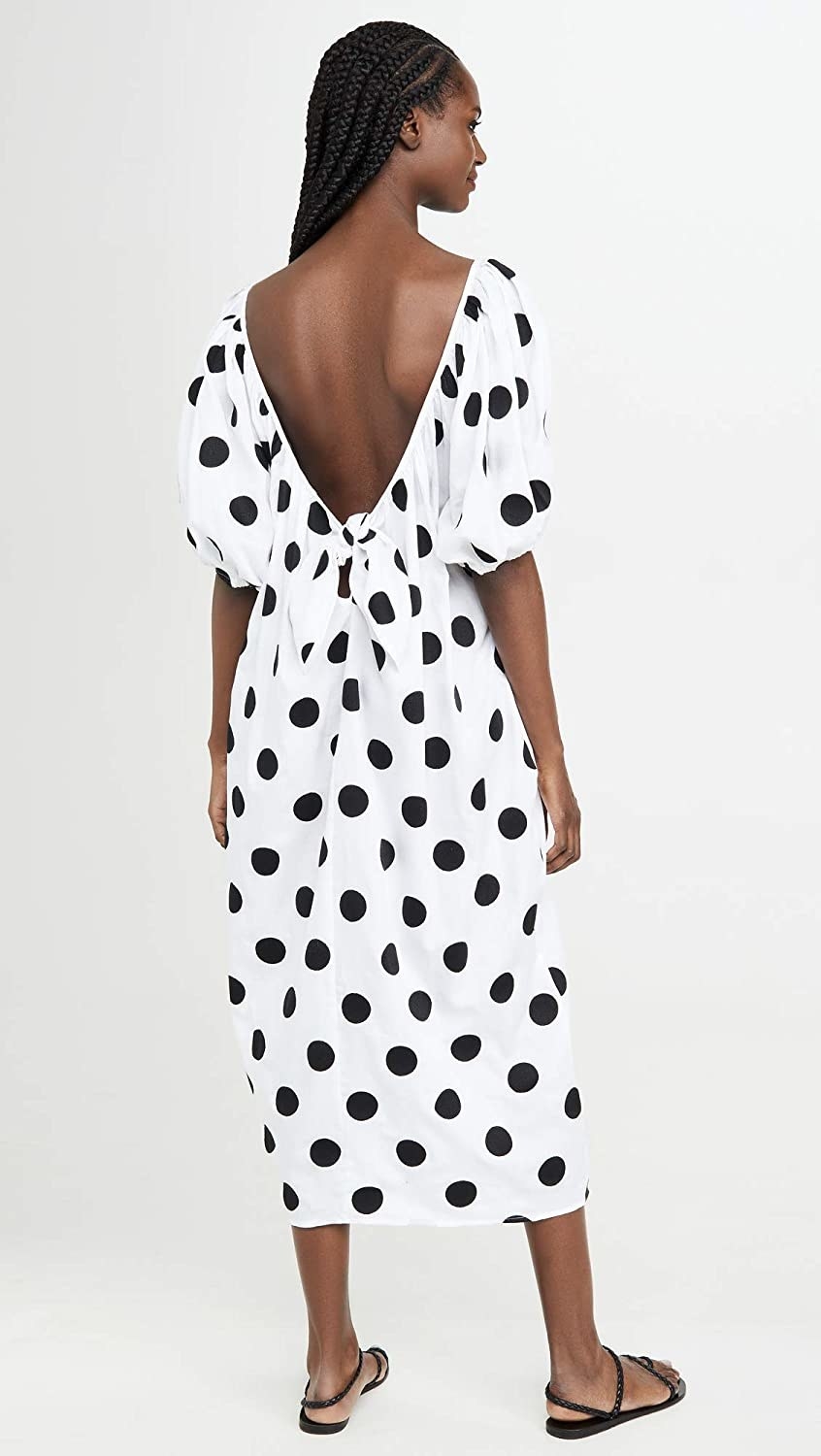 model shows back of white dress with black polka dots, deep plunge with bow at the bottom and puff sleeves