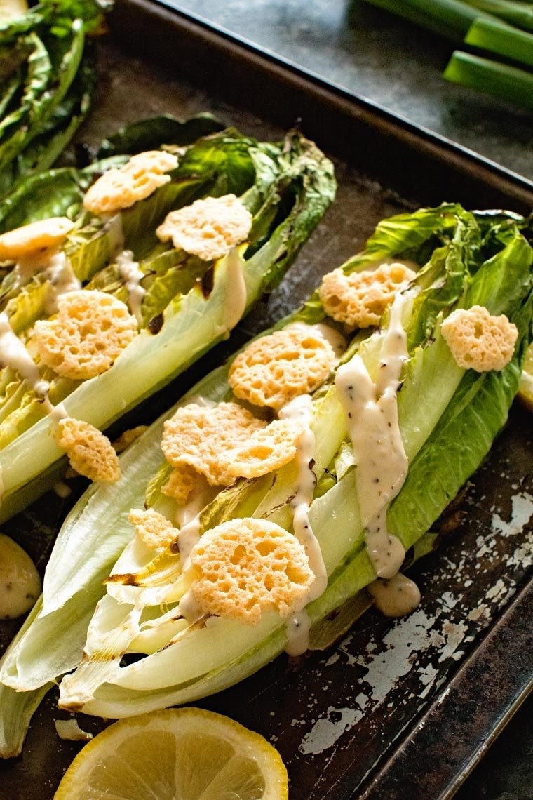 Two grilled romaine hearts drizzled with Caesar salad dressing and topped with Parmesan crisps.