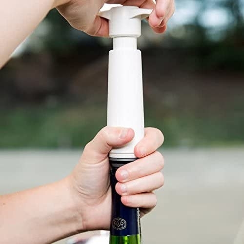 A hand uses the hand-held vacuum to pump air out of a glass bottle