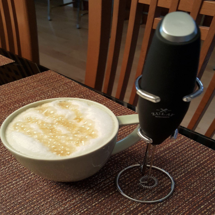 the thin black handheld frother next to a cup of coffee with foamy milk on top