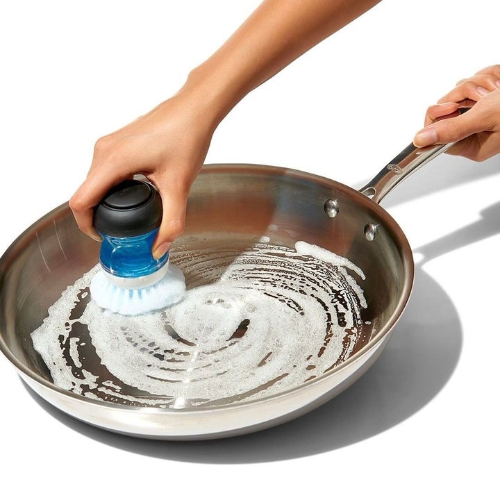 someone scubbing a soapy pan with the dish soap-filled brush that fits in their palm