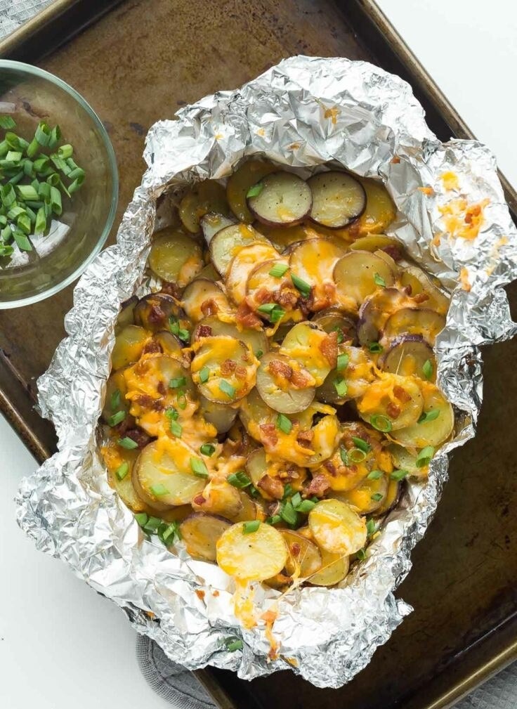 A foil packet full of grilled, sliced potatoes topped with cheese, bacon, and green onion.