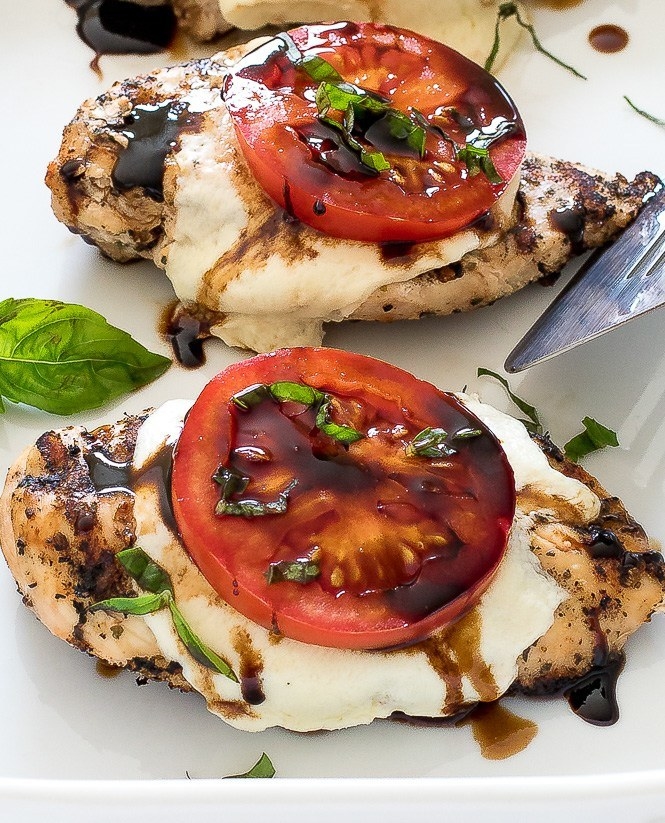 Three pieces of grilled chicken topped with melted mozzarella, a slice of tomato, shredded basil, and balsamic drizzle.