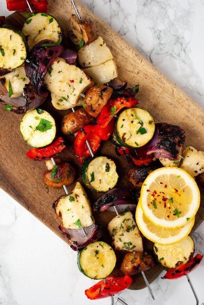 Three skewers of grilled halloumi cheese with onions, peppers, zucchini, and mushrooms.