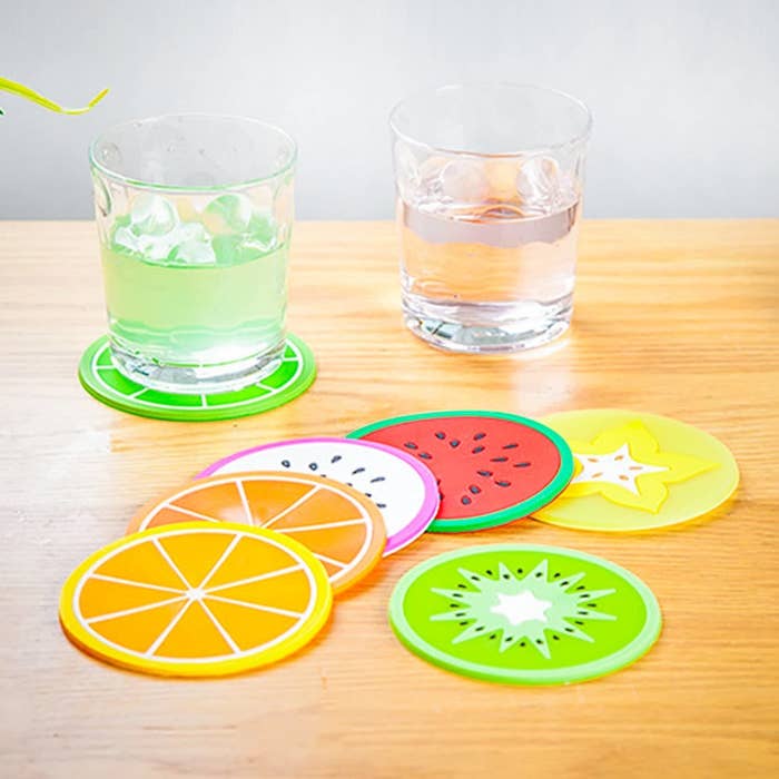 A set of round silicone coasters on a table They each look like a different sliced fruit