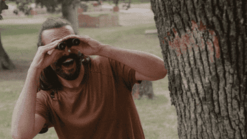A gif of Jonathan Van Nass smiling while using binoculars and then hiding behind a tree 