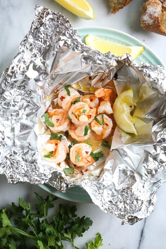 Shrimp in scampi sauce with fresh parsley and lemon wedges in a foil packet.