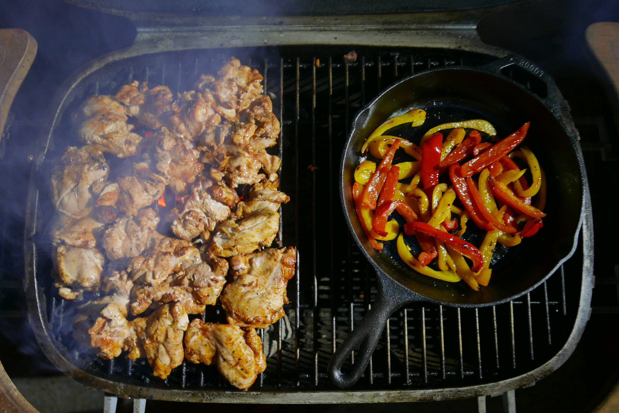 Chicken a cast iron skillet filled with bell peppers going on a grill.